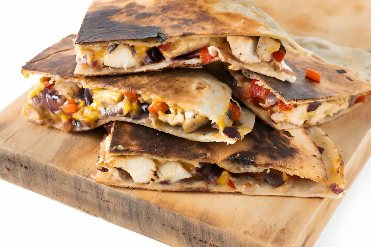 Stack of toasted quesadillas filled with chicken, vegetables, and melted cheese on a wooden board.