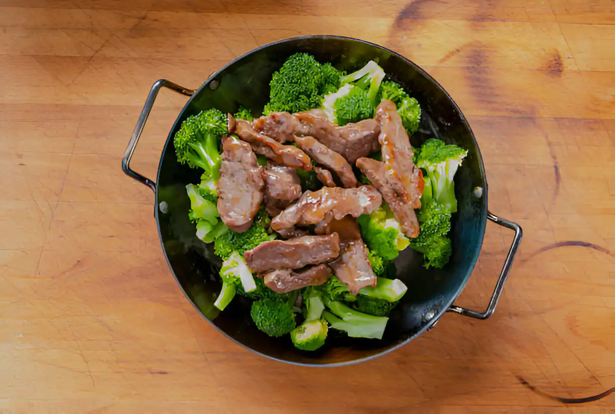 Stir-fried beef with broccoli in a black cooking pan on a wooden surface