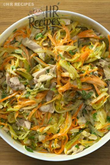 A colorful salad made with shredded vegetables and pieces of chicken in a white bowl on a wooden surface.
